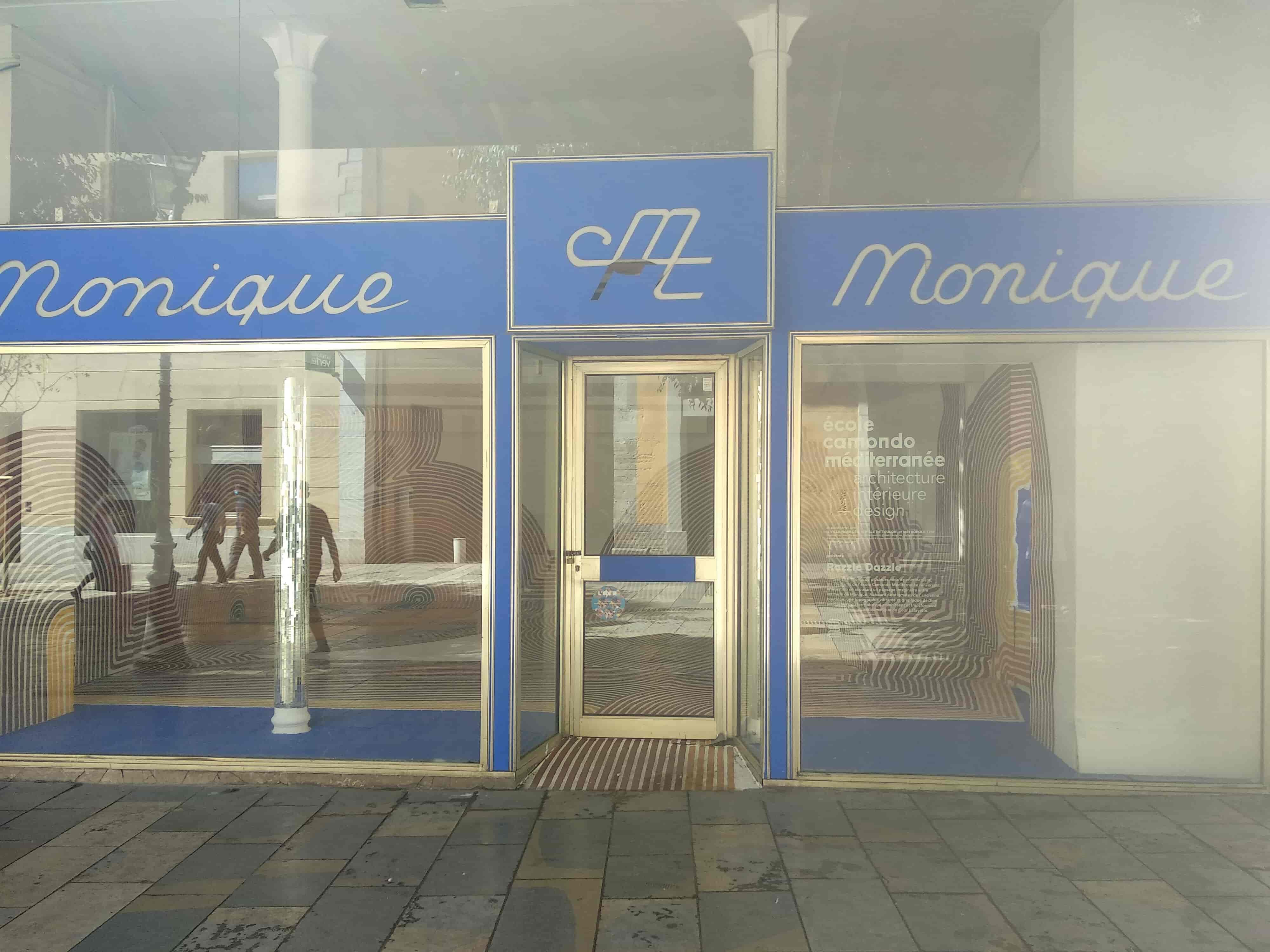 la devanture vitrée (des reflets de passants) d'une boutique vide, il reste le nom du magasin 'monique et monique'