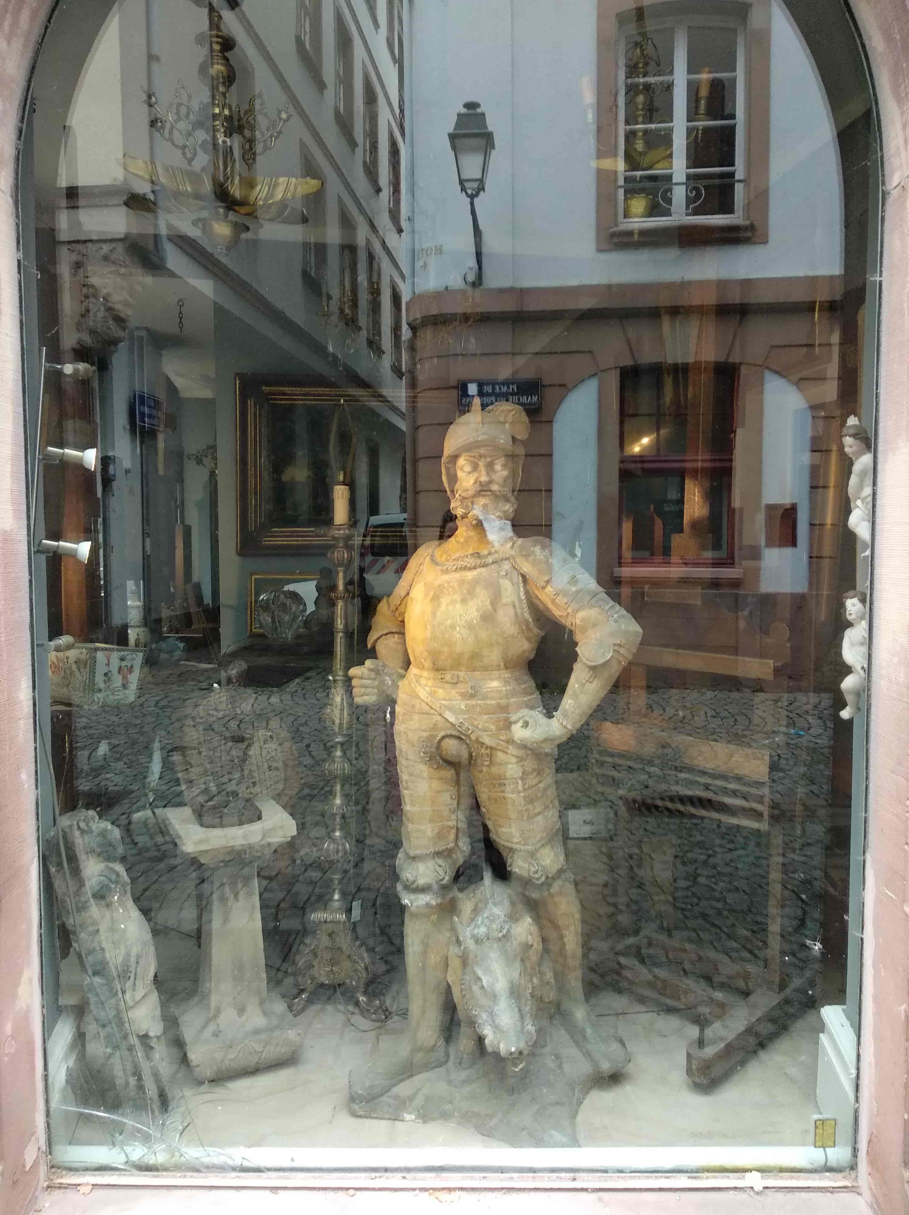 la vitrine d'un magasin d'antique où mon reflet est caché par une grande statue