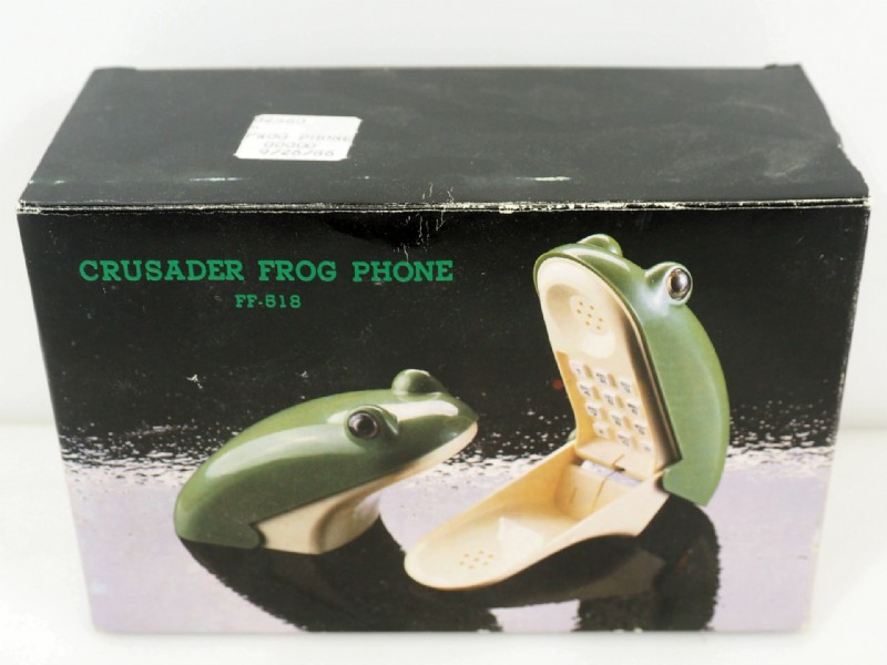 Une photo d'un vieux téléphone fixe en forme de grenouille, derrière sur la boîte est inscrit 'Crusader frog phone'.