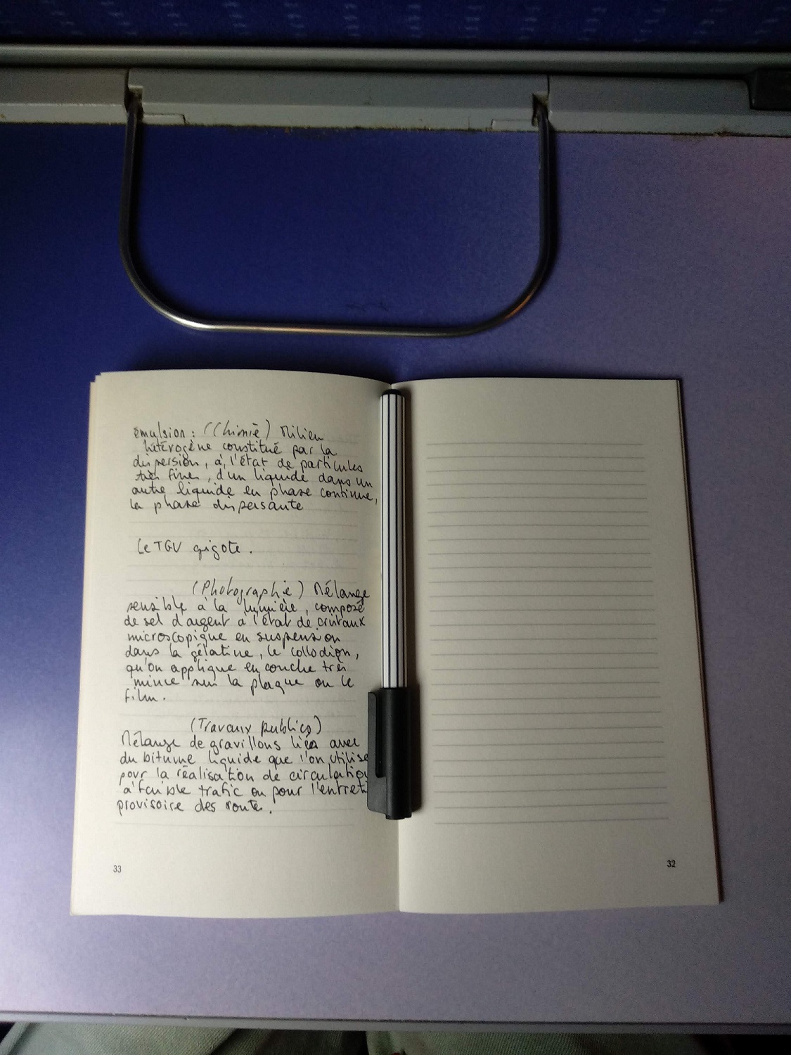 Une photo d'une page d'un carnet avec des définitions de l'émulsion, le carnet est posé sur une tablette de train